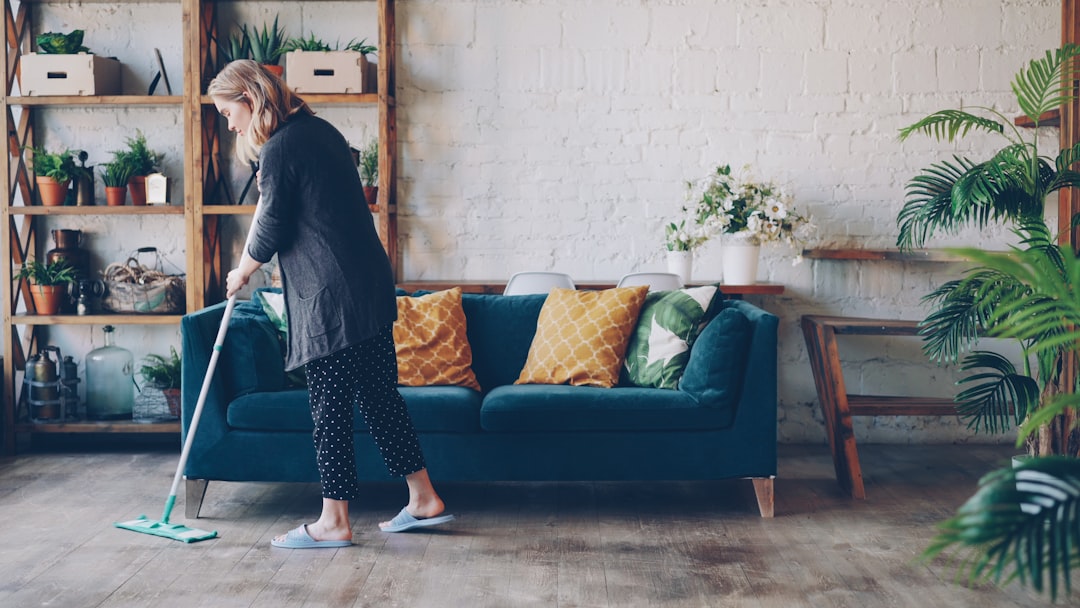 about-us Attractive young woman is cleaning living room mopping the floor doing housework. Beautiful loft style apartment with modern furniture and green plants is visible.